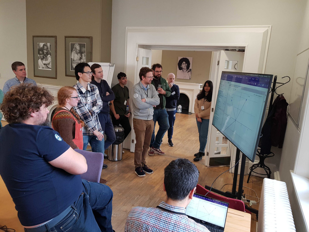 Photo of people crowding around a large TV with a Jupyter notebook showing an interactive example
